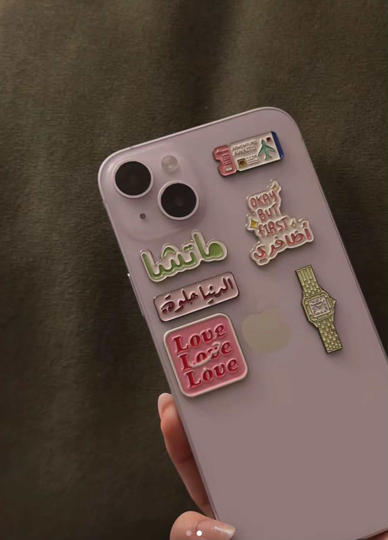 A lilac phone stacked with six metal stickers including matcha lettering, a Love Love Love square and a gold watch